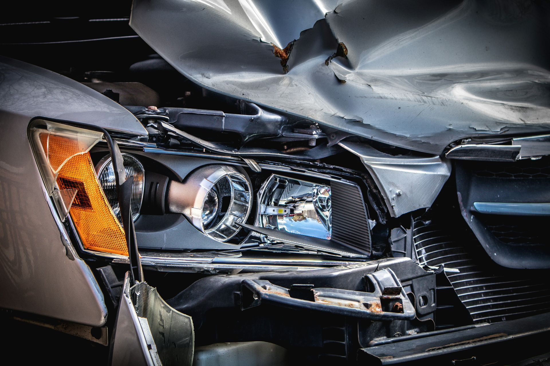 A damaged silver car with a crushed hood and broken headlight assembly
